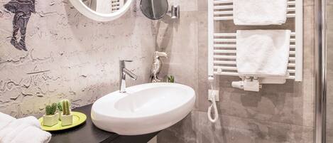 Une salle de bain moderne avec un miroir rond, un lavabo blanc, un porte-serviettes et un espace douche.