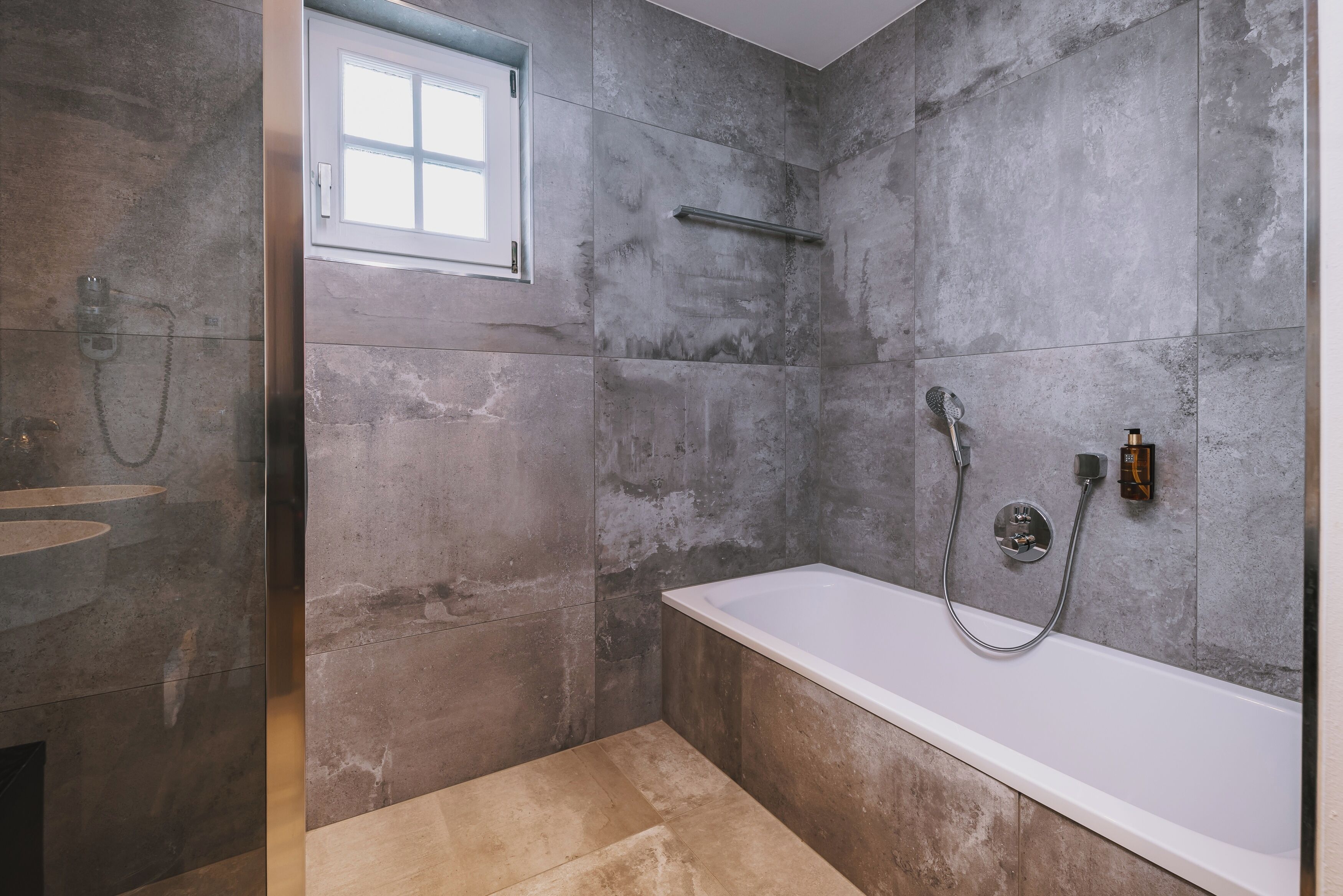 A modern bathroom with a bathtub, shower, and a window.