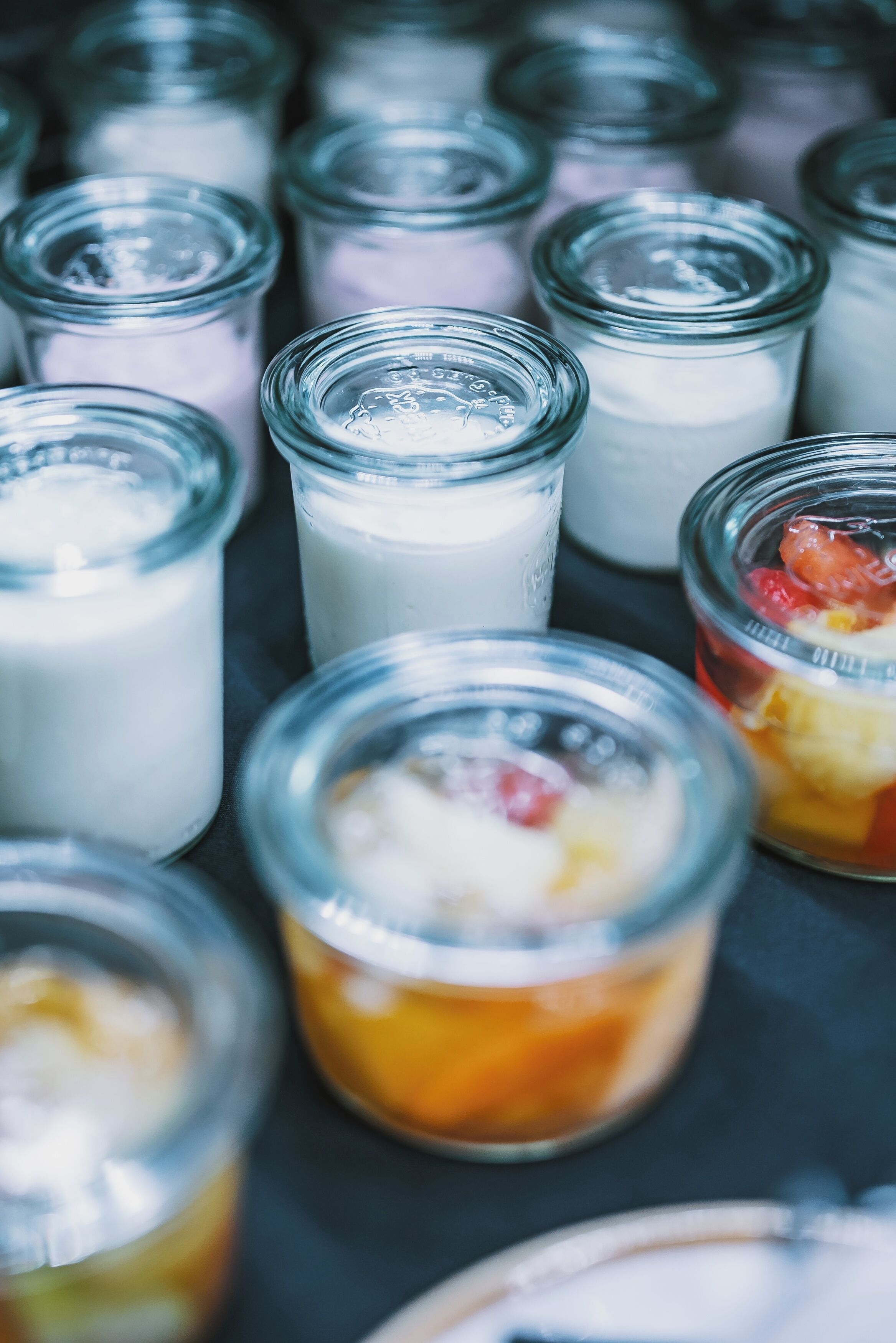 Variedad de pequeños frascos de vidrio con diferentes alimentos, probablemente productos lácteos o postres, dispuestos sobre una superficie.