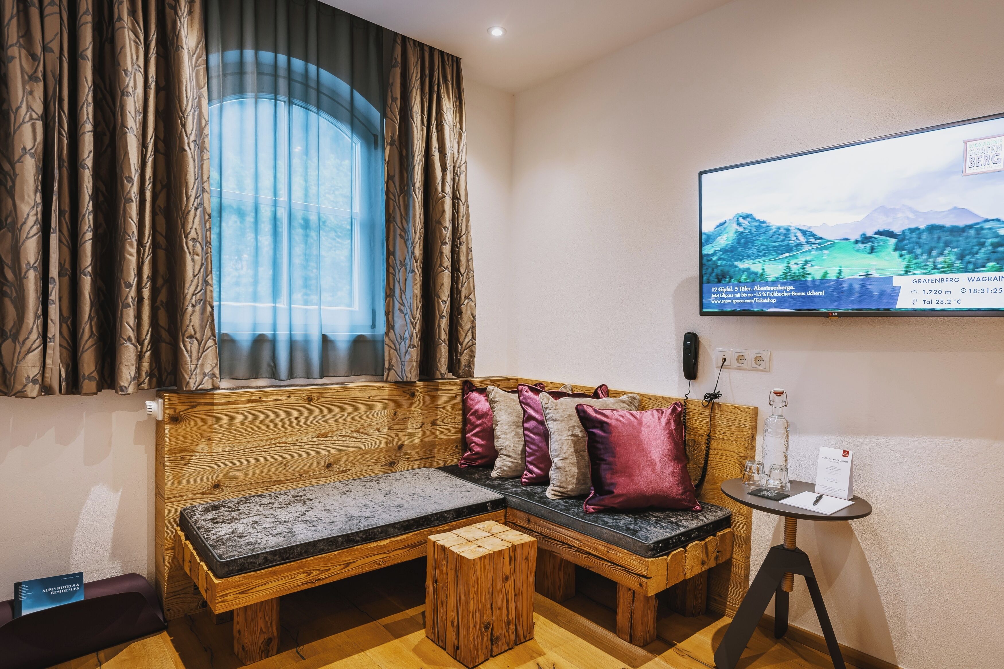 Una habitación acogedora con un banco de madera, una mesita con una botella y un televisor mostrando una vista panorámica.