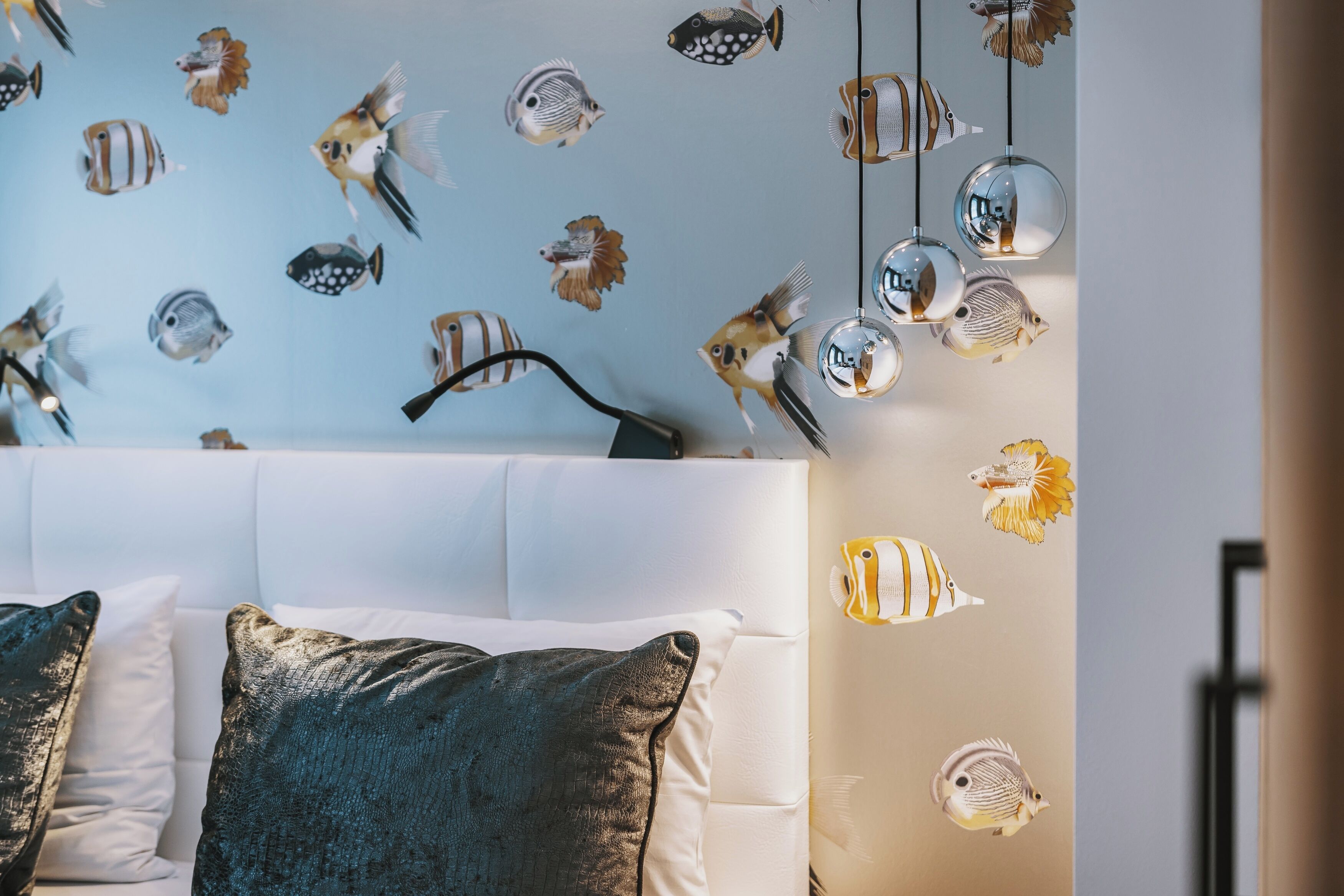 A bedroom with a white headboard, decorative fish wall decals, and hanging spherical light fixtures.