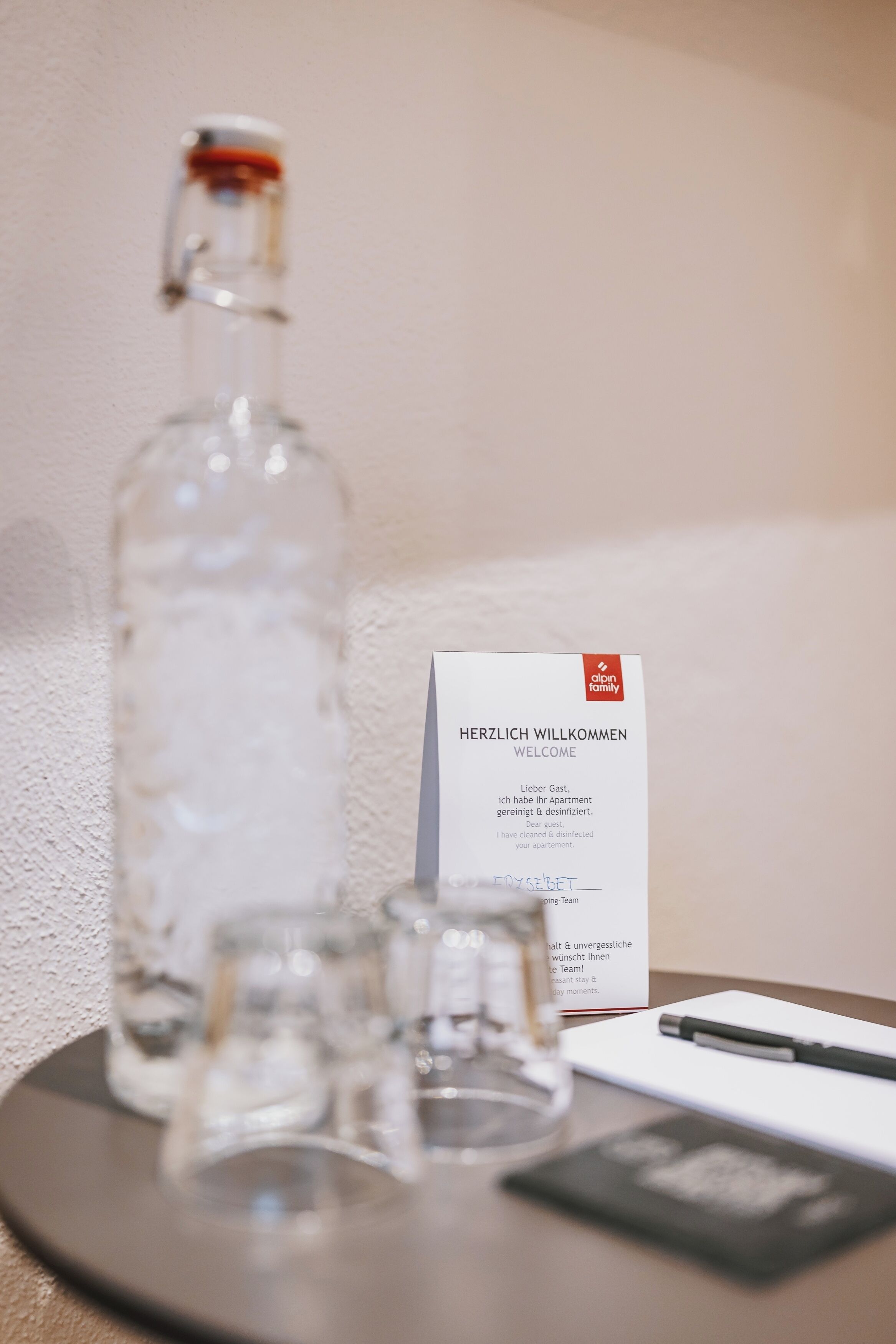Una mesa con una botella, vasos, una tarjeta de bienvenida y un bolígrafo.