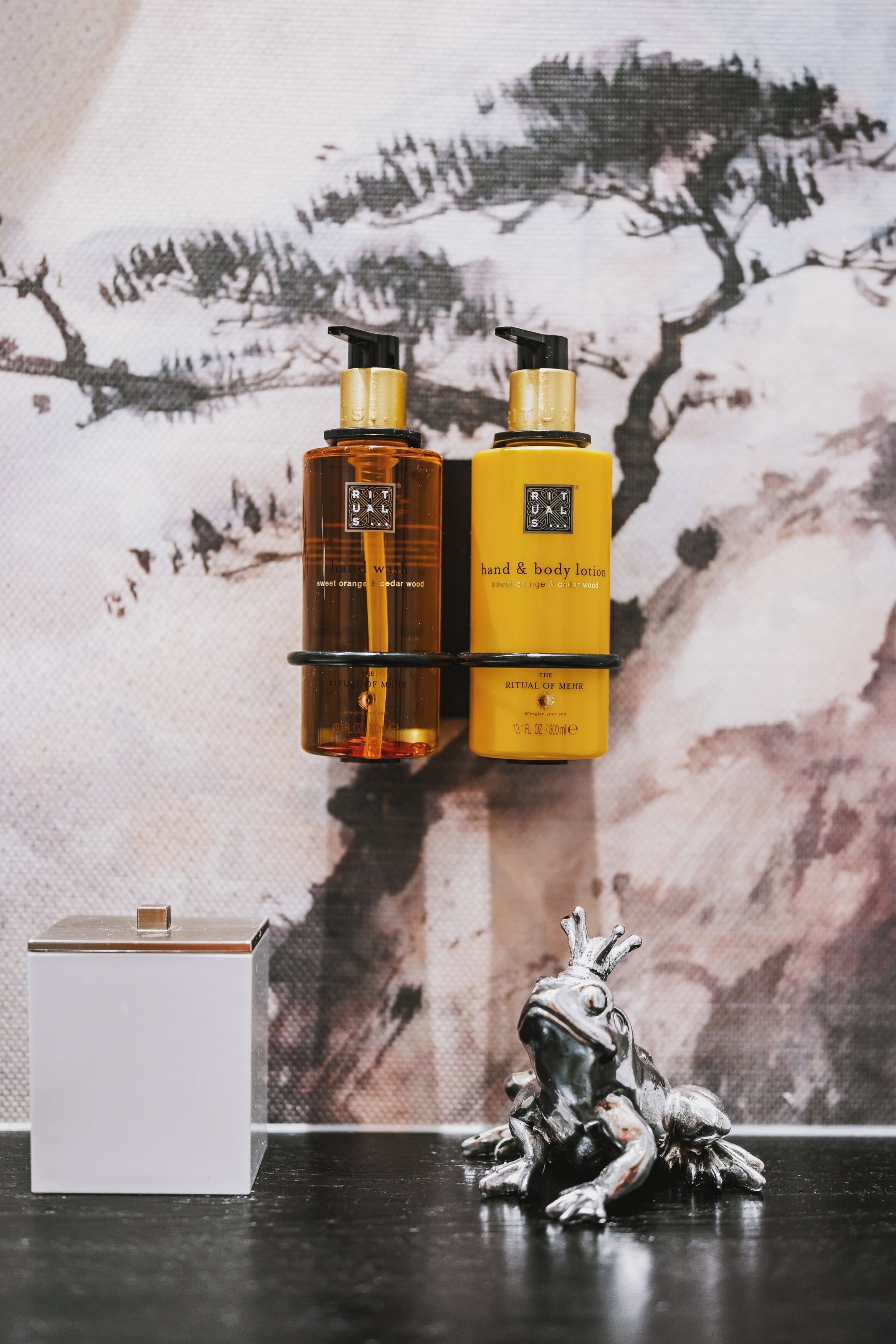 Deux flacons de lotion pour les mains et le corps, posés sur un mur dont le fond est texturé.
