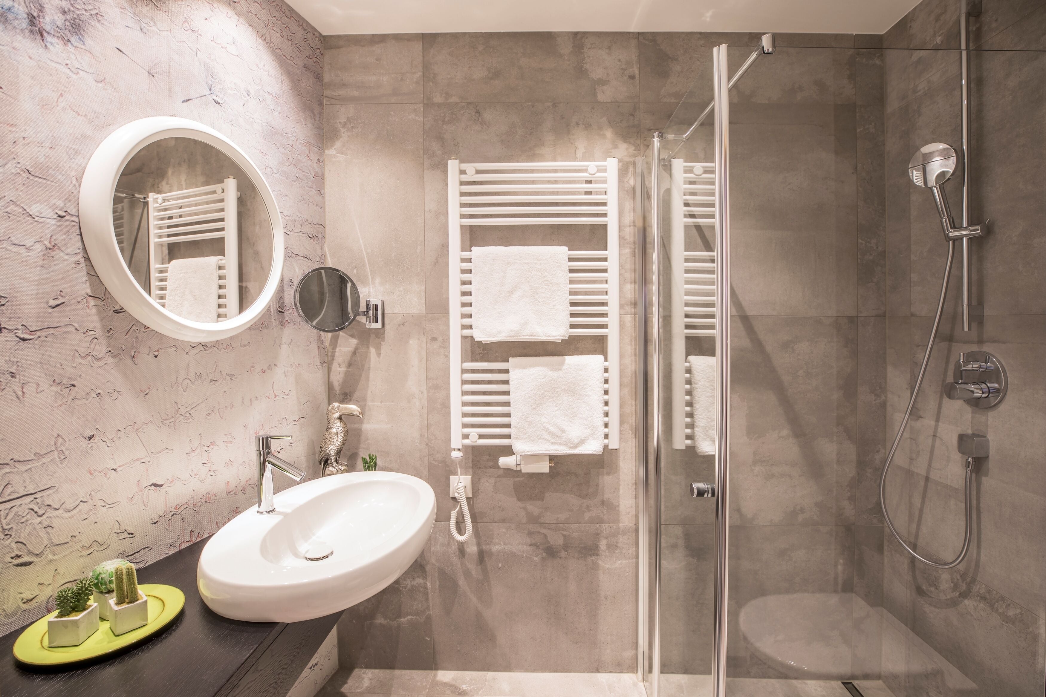 A modern bathroom with a glass-enclosed shower, a round mirror, and a white sink.