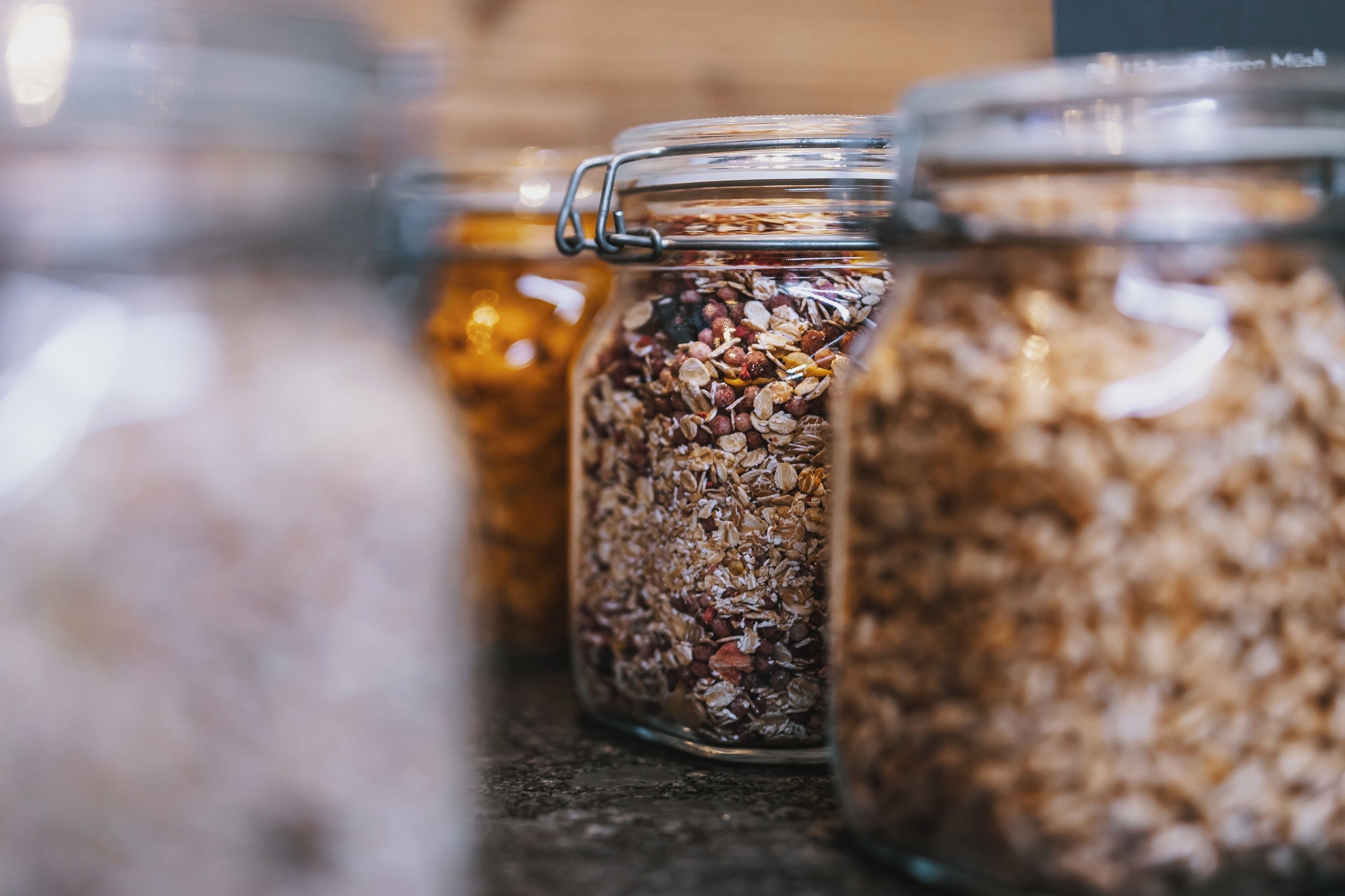 Tres frascos de vidrio repletos de diferentes cereales y semillas, dispuestos sobre una encimera.