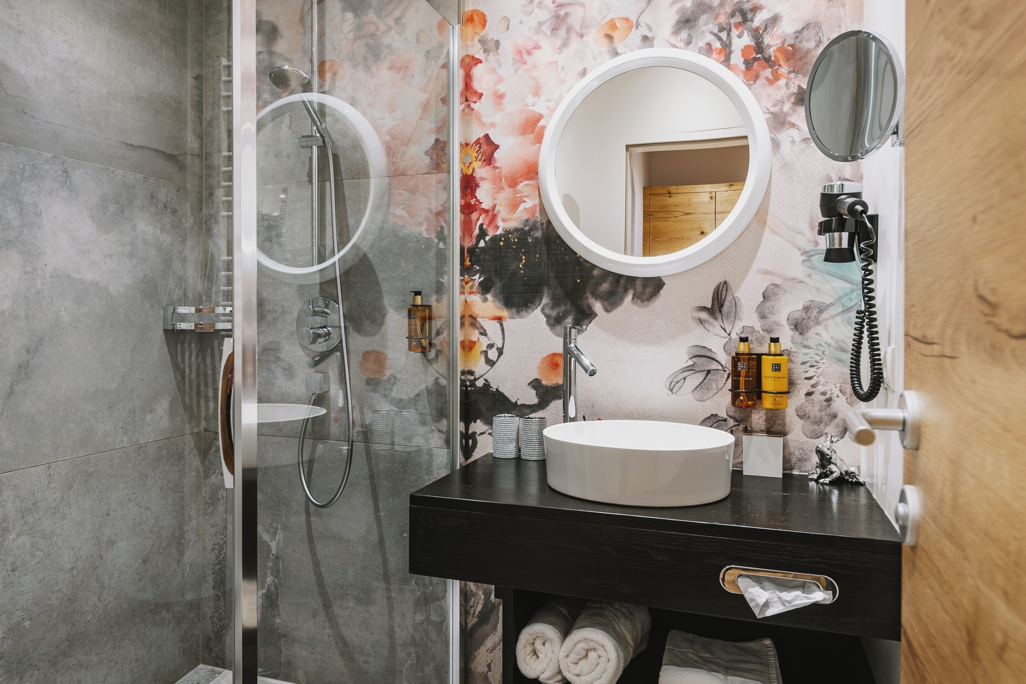 A bathroom with a glass-enclosed shower, a round sink with a mirror, and a wooden door.