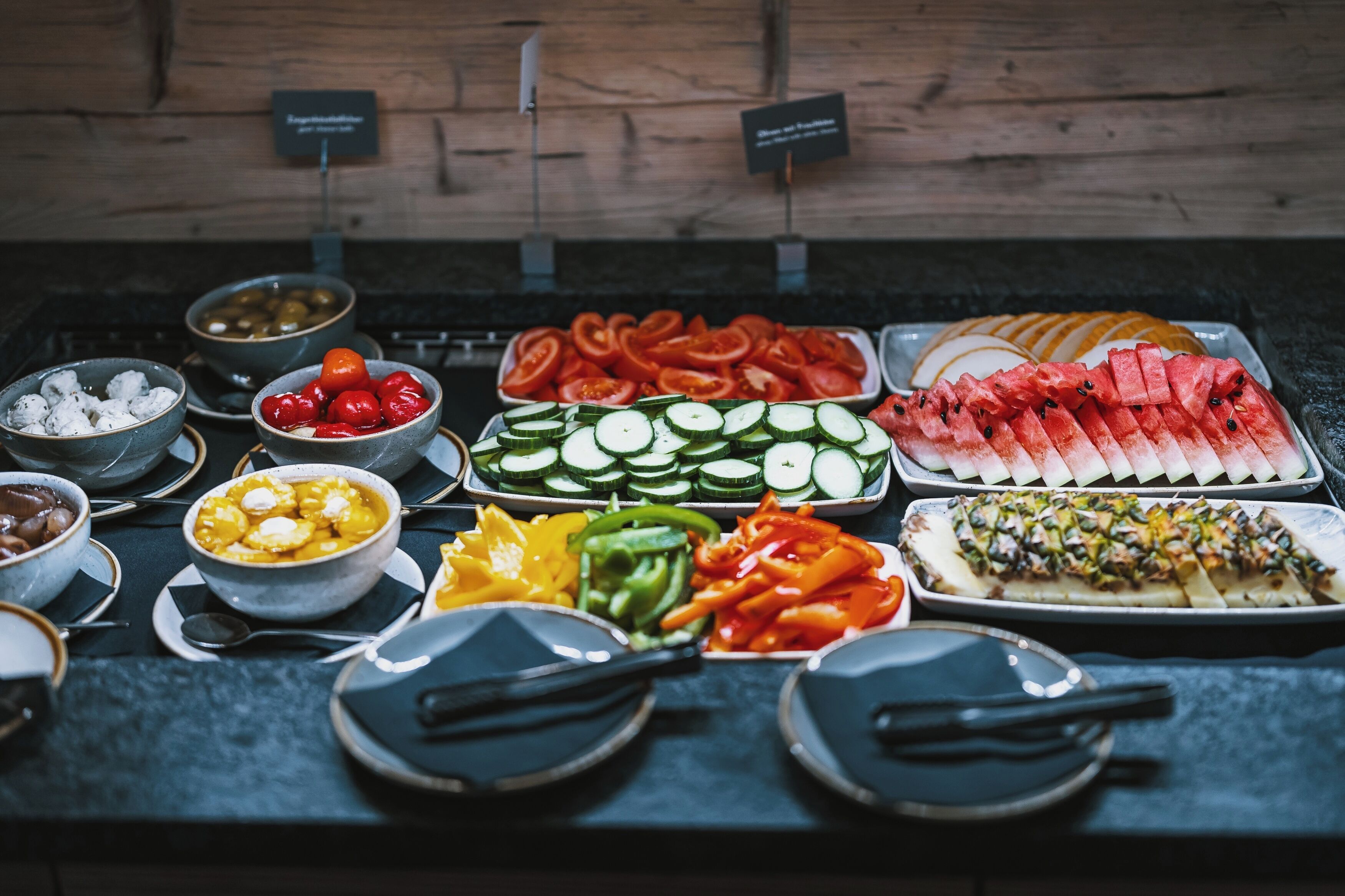 Ein Buffet mit verschiedenen Speisen, darunter Gurkenscheiben, Tomaten und Wassermelone.