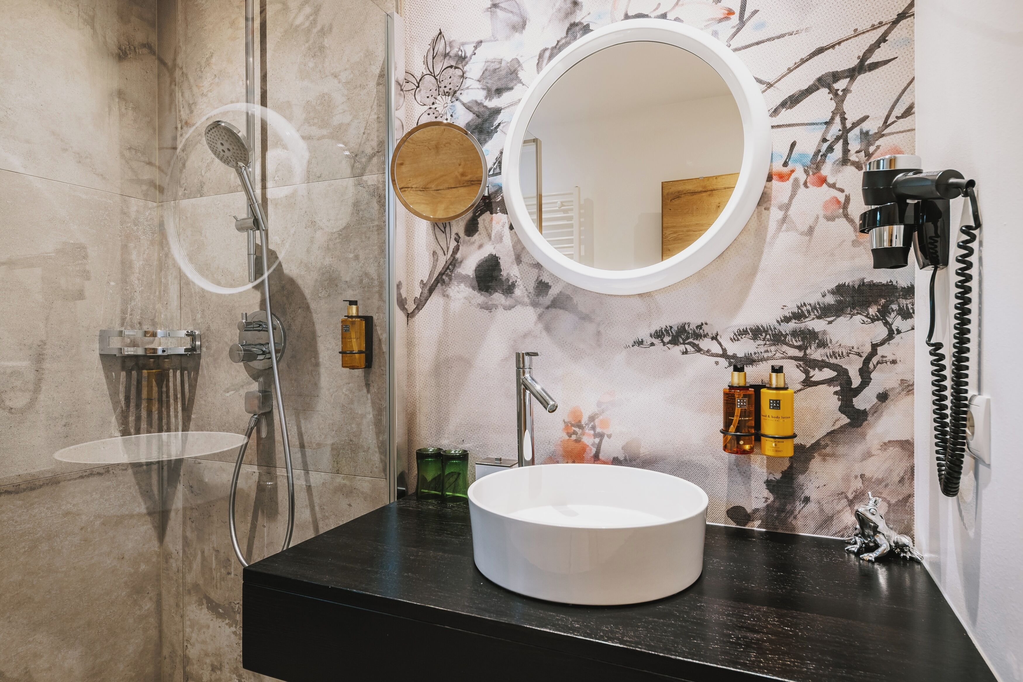 Een badkamer met een ronde spiegel, een wastafel en een douche.