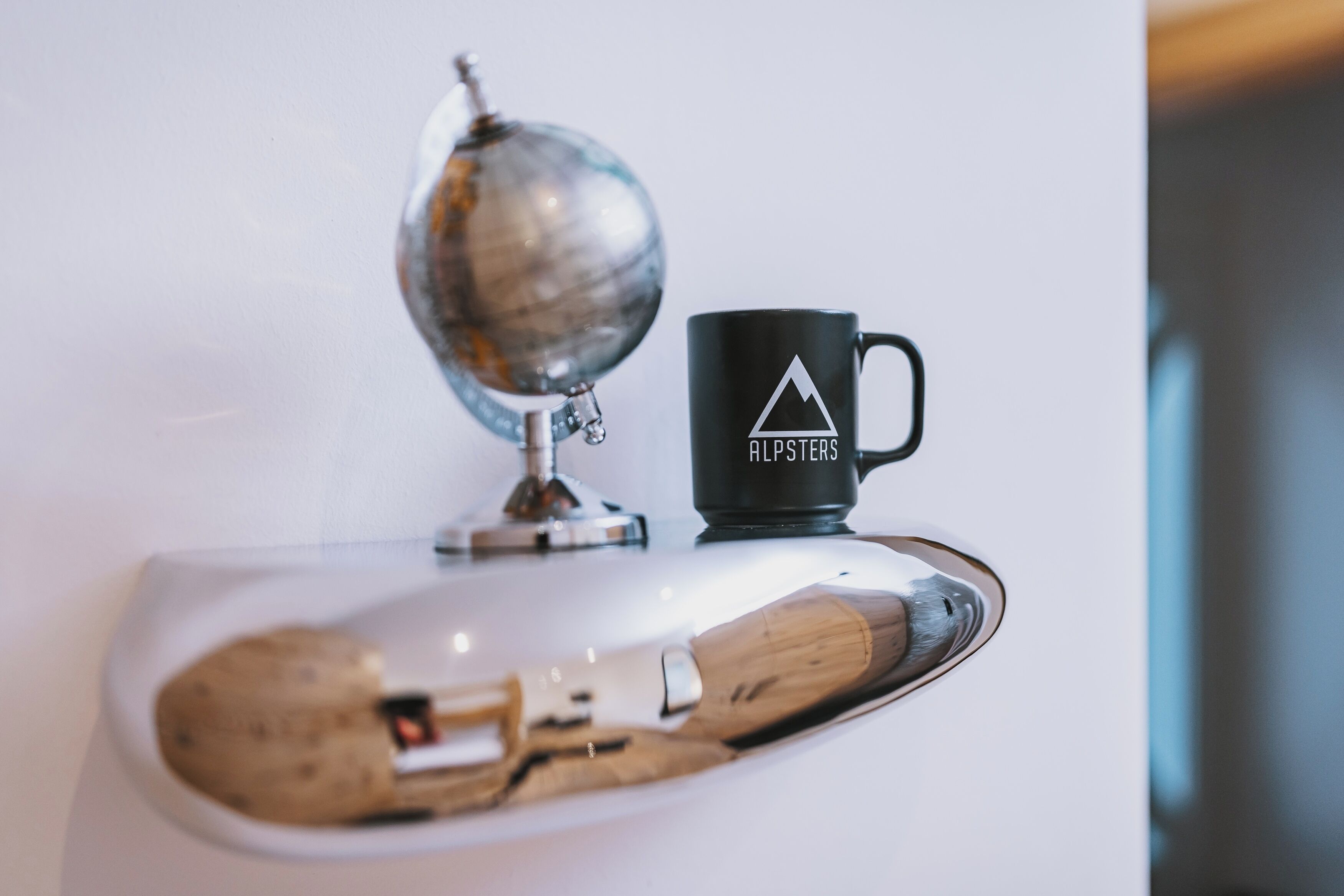 A globe, a black mug with a mountain logo, and a wooden spoon on a white surface.