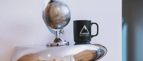 A globe, a black mug with a mountain logo, and a wooden spoon on a white surface.