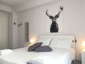 A bedroom with a bed, pillows, a bedside table, a lamp, and a wall-mounted mirror.
