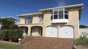 A two-story house with a front garage, a balcony on the upper floor, and a well-maintained lawn. - Tiro Moana beautifully renovated pet friendly home (Forster)