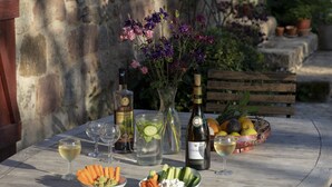 Een gedekte tafel met een fles wijn, glazen, een schaal groenten, een vaas met bloemen en een mand vol fruit.