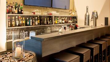 Una zona de bar con estanterías llenas de botellas de licor, vasos y taburetes.
