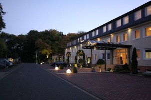 A modern hotel with a brick pathway leading to the entrance, surrounded by well-maintained landscaping and parked cars.