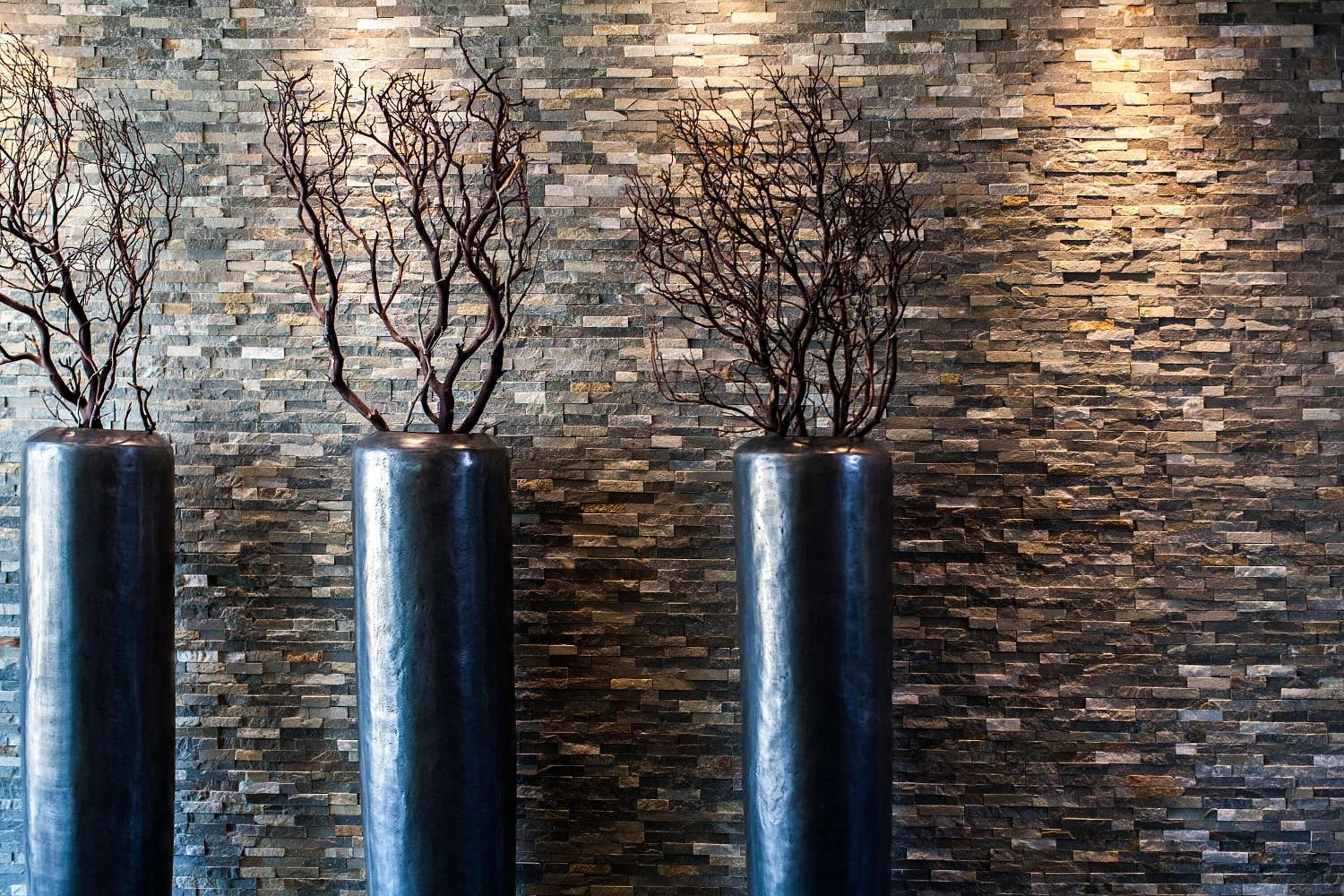 Three cylindrical vases with branches against a textured stone wall.
