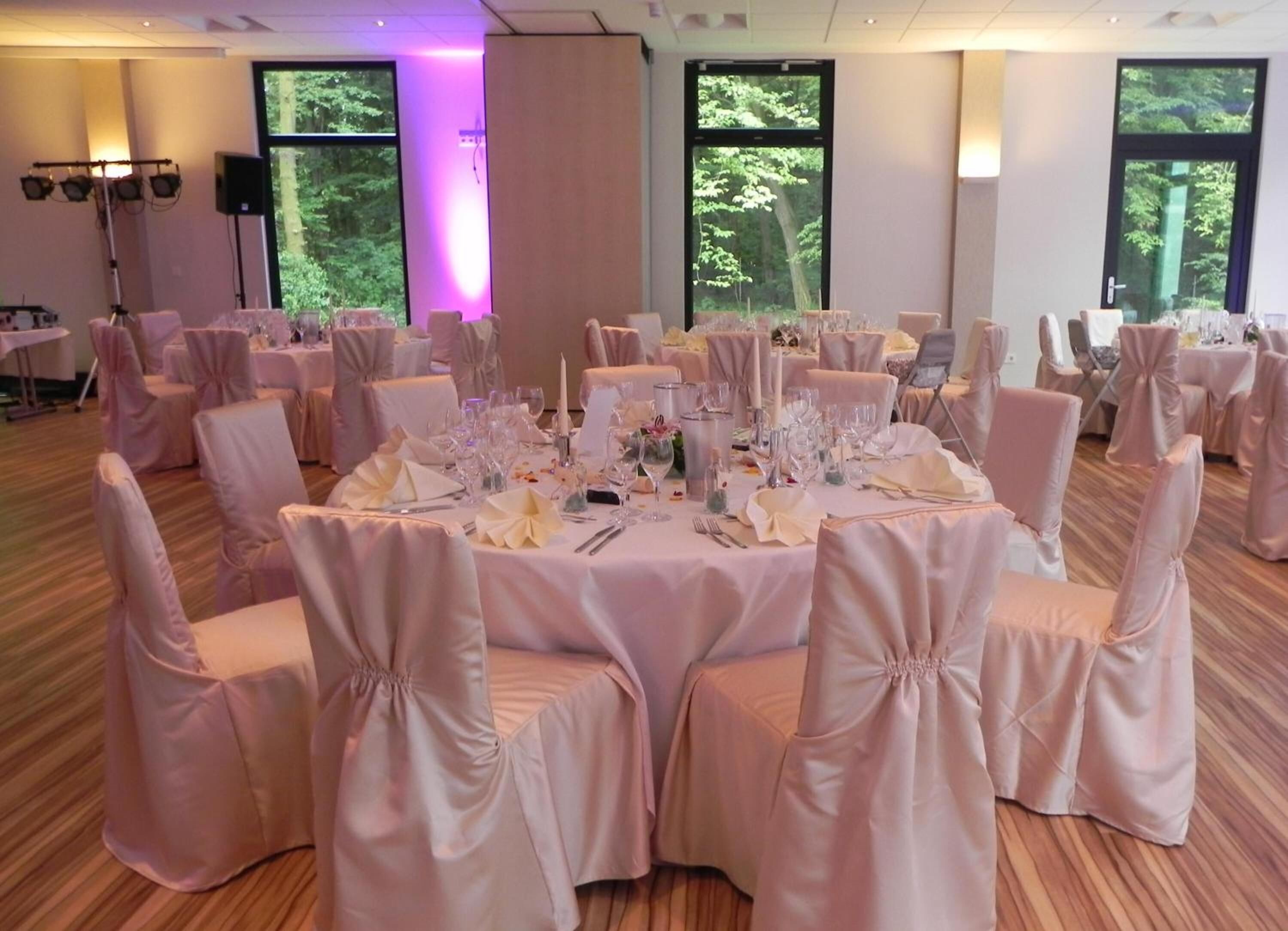 A banquet hall with round tables set for a formal event, featuring white tablecloths and matching chair covers.