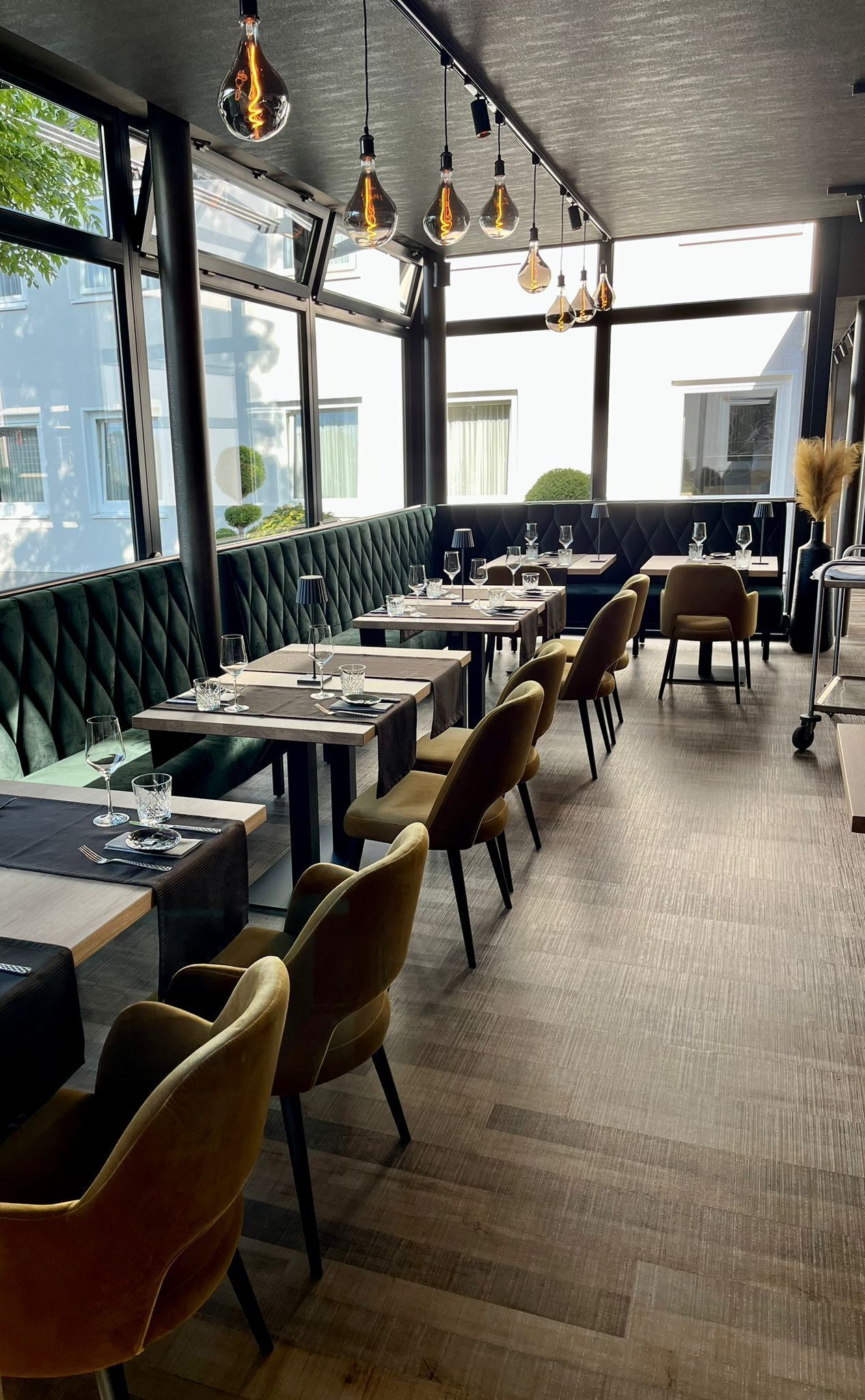 A restaurant with high tables and booths, modern pendant lighting, and large windows offering views of the outside.