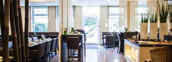 A modern restaurant with multiple dining tables and chairs, large windows, and a well-lit interior.