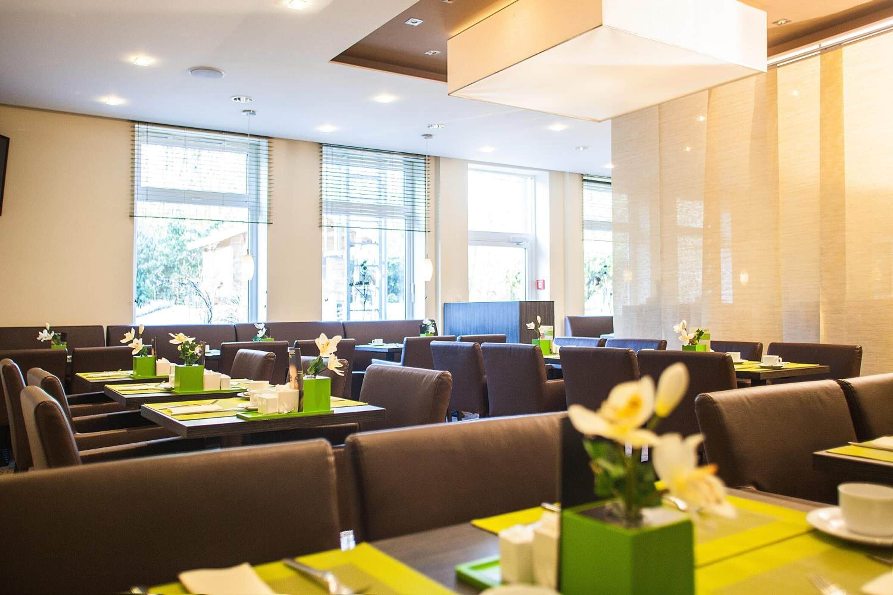 Un espace repas moderne avec des banquettes et des tables, chacune agrémentée de sets de table verts et de fleurs blanches.