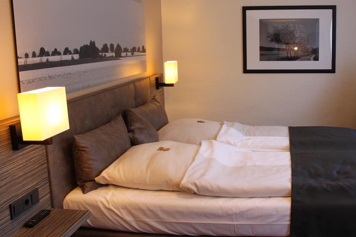 Ein ordentlich bezogenes Bett mit Kopfteil, zwei Nachttischlampen und einem gerahmten Bild an der Wand.