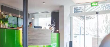 A reception area with a green counter, a receptionist, and a large window providing a view of the outside.