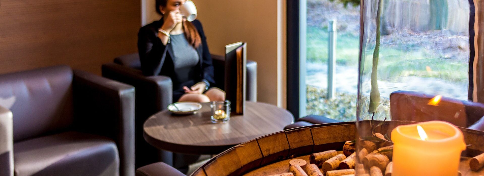 A cozy indoor setting with leather seating, a table with a candle and a glass, and a view of greenery outside.
