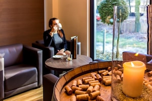 A cozy indoor setting with a round wooden table holding wine corks, a lit candle, and a glass of water.