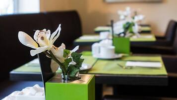 Un ambiente de restaurante con manteles individuales verdes, vajilla blanca y una sola orquídea decorando cada mesa.