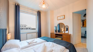 A hotel room with a bed, a desk, a mirror, and a window with curtains. - Apartamenty Sun&Snow Reymonta (Kolobrzeg)
