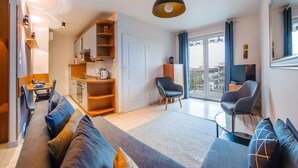 A modern living room with a sofa, a dining area, a kitchen, and a balcony with a view. - Apartamenty Sun&Snow Reymonta (Kolobrzeg)