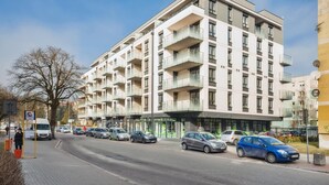 A multi-story residential building with balconies, a parking area with cars, and a clear sky. - Apartamenty Sun&Snow Reymonta (Kolobrzeg)