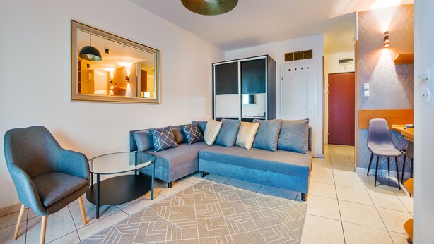 A modern living room with a sectional sofa, a glass coffee table, and a blue armchair. - Apartamenty Sun&Snow Reymonta (Kolobrzeg)
