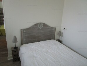 Une chambre à coucher avec une tête de lit en bois, une table de chevet avec une lampe et un couvre-lit blanc.