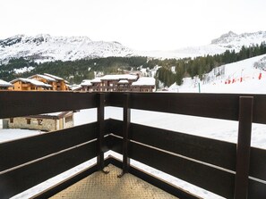 Een balkon met uitzicht op besneeuwde bergen en een skipiste.