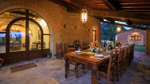 An outdoor dining area with a stone floor, wooden tables and chairs, and a brick wall. - Podere Maiano - Private Pool Villa with 9 Bdrs and Spa (Buonconvento, Siena)