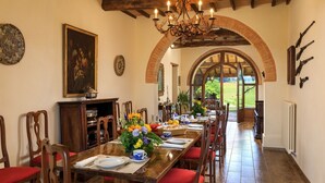 A dining room with a long wooden table set for a meal, flanked by chairs with red cushions. An ornate chandelier hangs from the ceiling, and a large painting is visible on the wall. - Podere Maiano - Private Pool Villa with 9 Bdrs and Spa (Buonconvento, Siena)