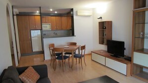 Un espace de vie compact comprenant un coin cuisine, un coin repas, un canapé, un téléviseur et une bibliothèque.