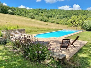 Une piscine entourée de chaises longues, elle-même bordée d’un jardin et d’une colline.