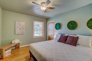 Quarto com cama, ventoinha no teto, janela com persianas e duas obras de arte nas paredes.