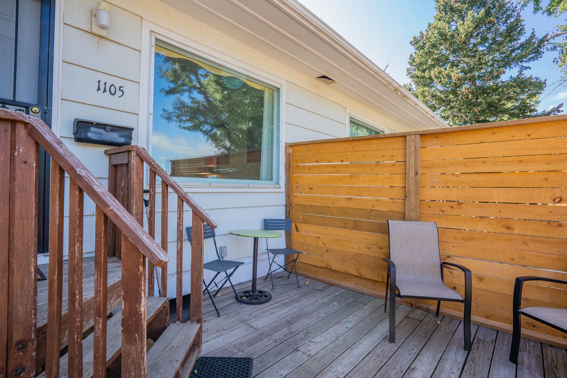 A wooden deck with a wooden fence, a small table, and two chairs.