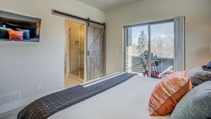 A bedroom with a bed, a sliding door to a bathroom, a large window with a view of outdoor skis, and a TV mounted on the wall. - 4BR Mnt Viewsmodern Urbanityrooftop Patio (Colorado Springs)