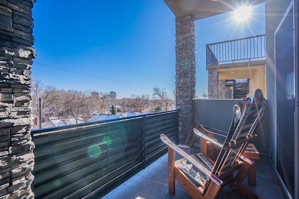 A balcony with a stone wall, a wooden chair, and skis leaning against the wall.