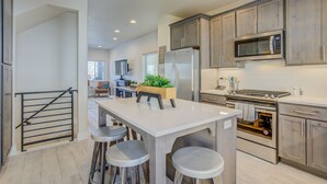 A modern kitchen with stainless steel appliances, a central island with stools, and wooden cabinets. - 4BR Mnt Viewsmodern Urbanityrooftop Patio (Colorado Springs)