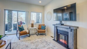 A modern living room with a fireplace, a flat-screen TV, and a stone pillar. - 4BR Mnt Viewsmodern Urbanityrooftop Patio (Colorado Springs)