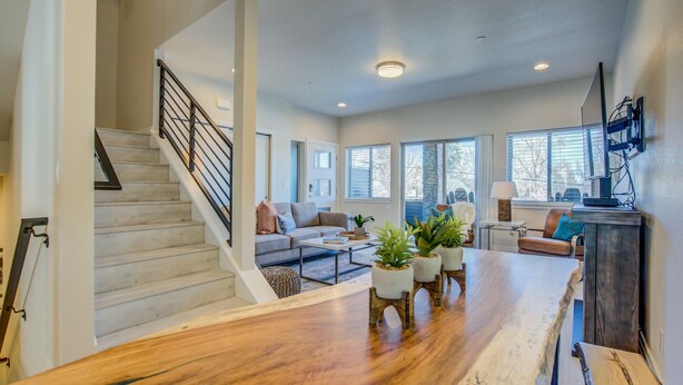 A spacious living area with a wooden coffee table, a sofa, and a TV. There is a staircase with a railing and a door leading to another room. - 4BR Mnt Viewsmodern Urbanityrooftop Patio (Colorado Springs)