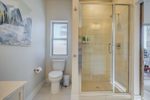 A bathroom with a toilet, a glass-enclosed shower, and a window.