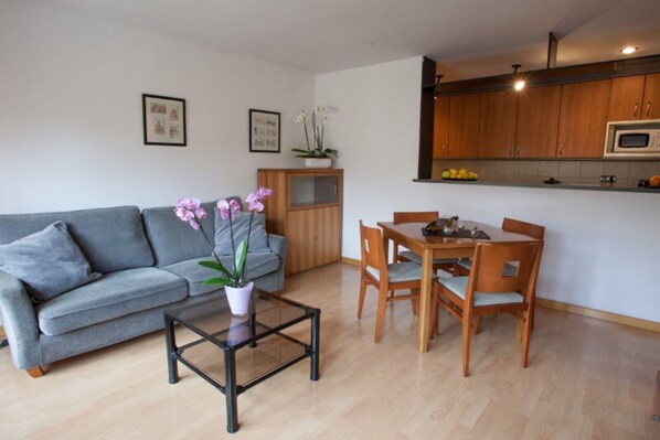 A modern living room with a grey sofa, a glass coffee table, and a dining area with wooden chairs and a table.