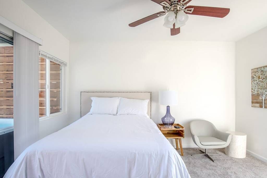 A bedroom with a bed, a nightstand, a chair, a ceiling fan, and a window.