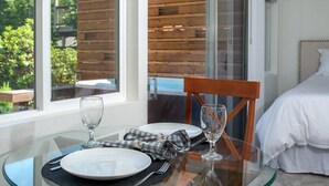 Ein Esstisch ist gedeckt mit Tellern, Gläsern und einer karierten Serviette, nahe einem Fenster mit Blick auf eine Holzterrasse und Grünflächen.